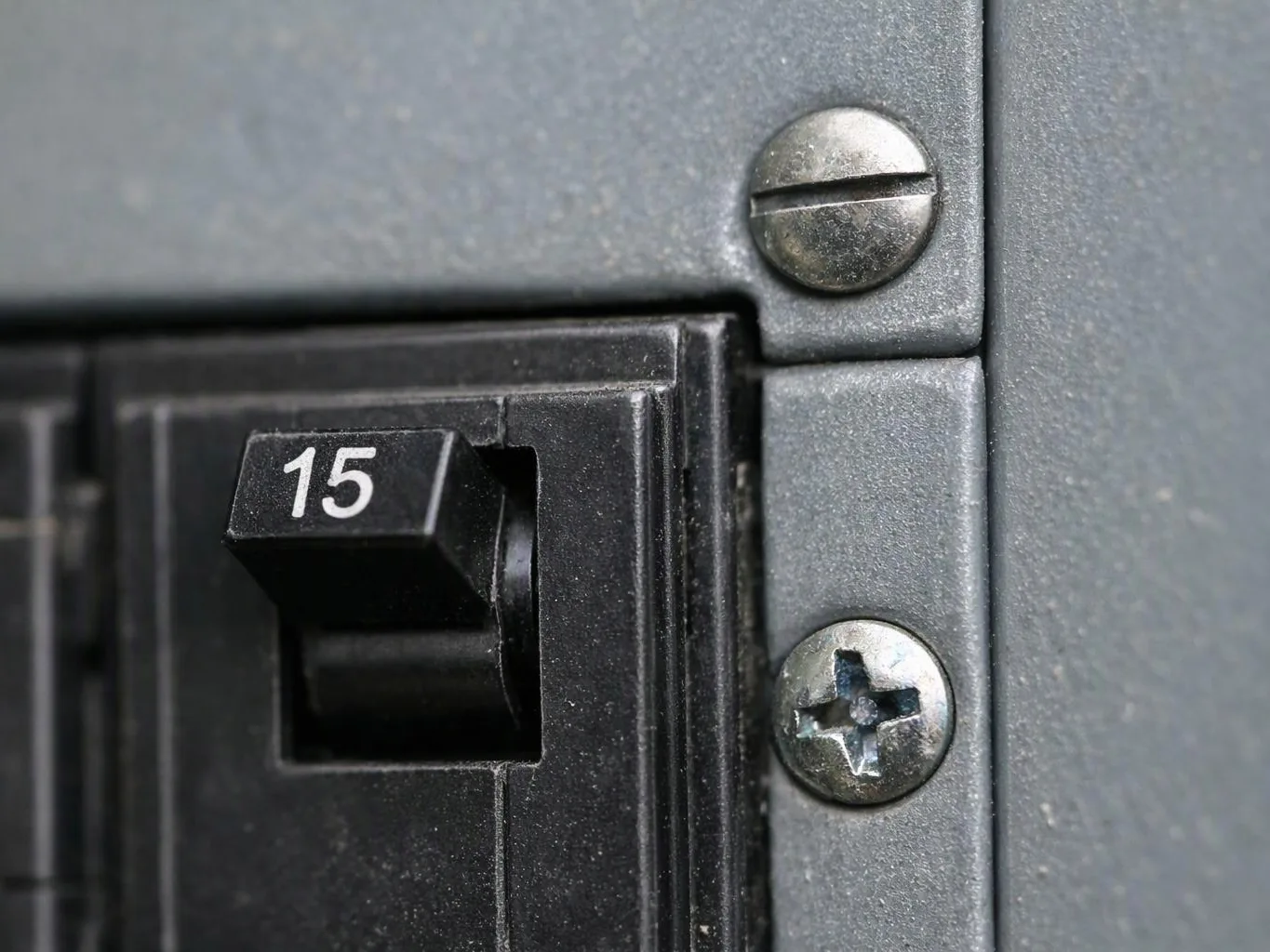 Close-up of a black circuit breaker labeled 15 beside gray panel screws