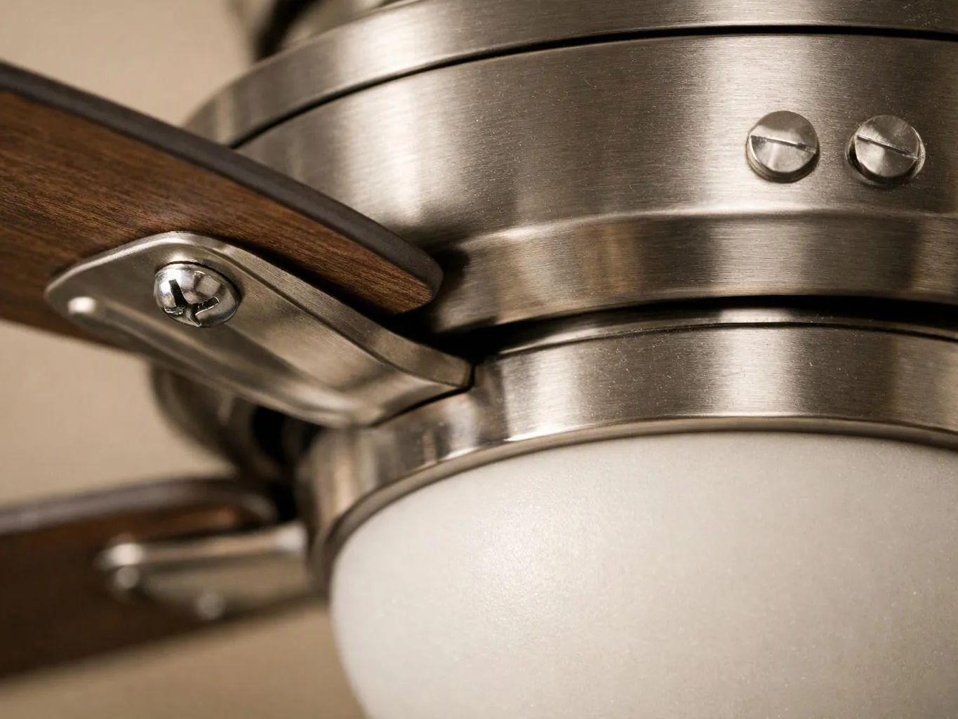 Close-up of a brushed metal ceiling fan with a wood blade and frosted light globe