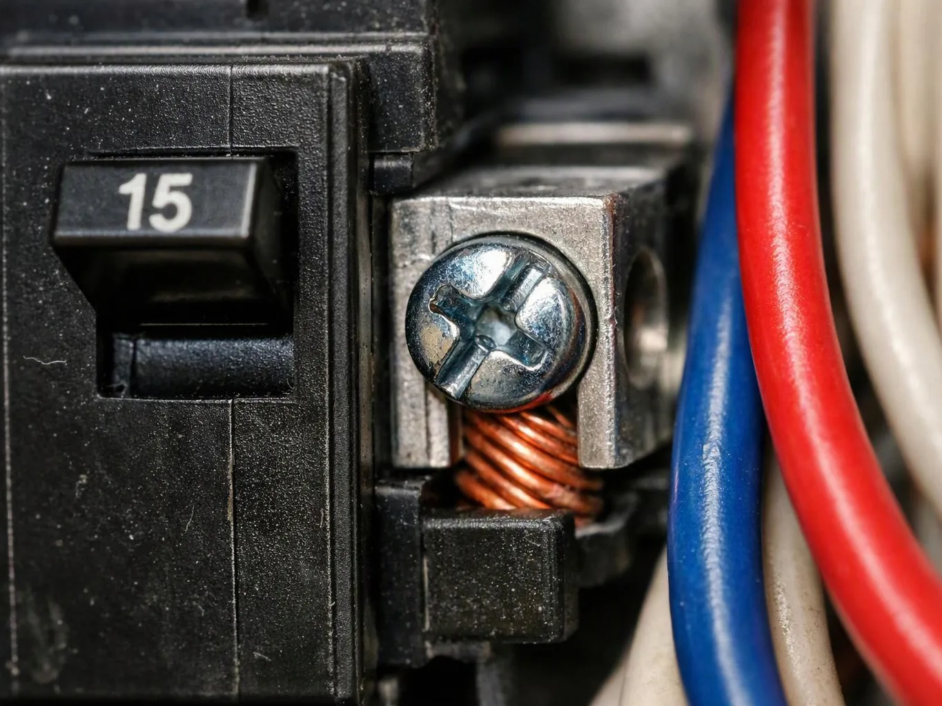 Close-up of an electrical breaker with a visible 15 label, screw terminal, and colored wires attached