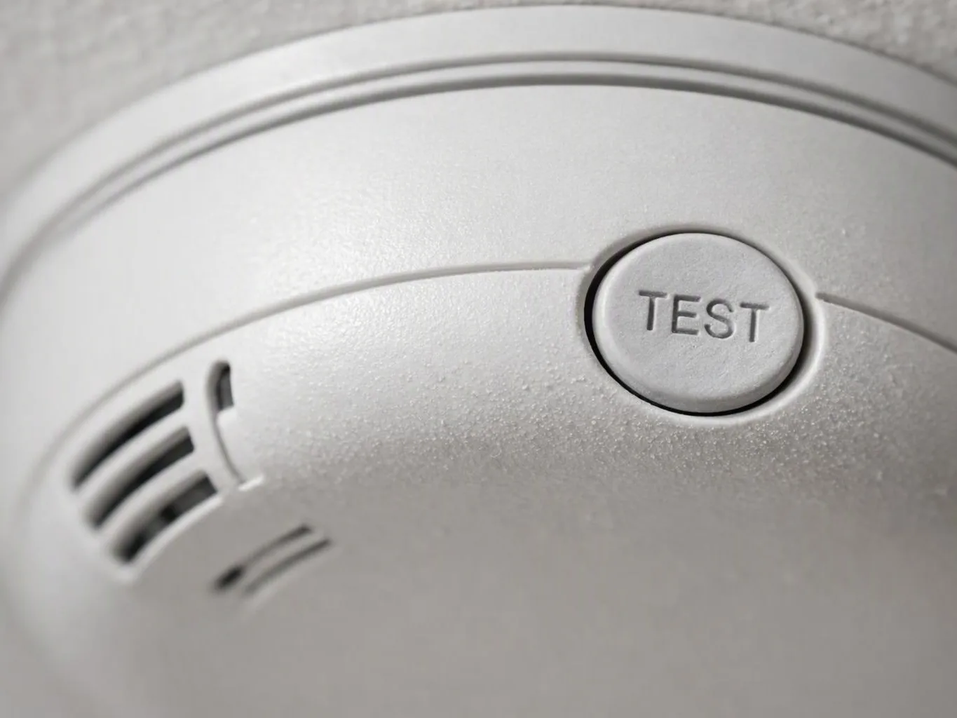 Close-up of a white smoke detector with a TEST button and vent slots