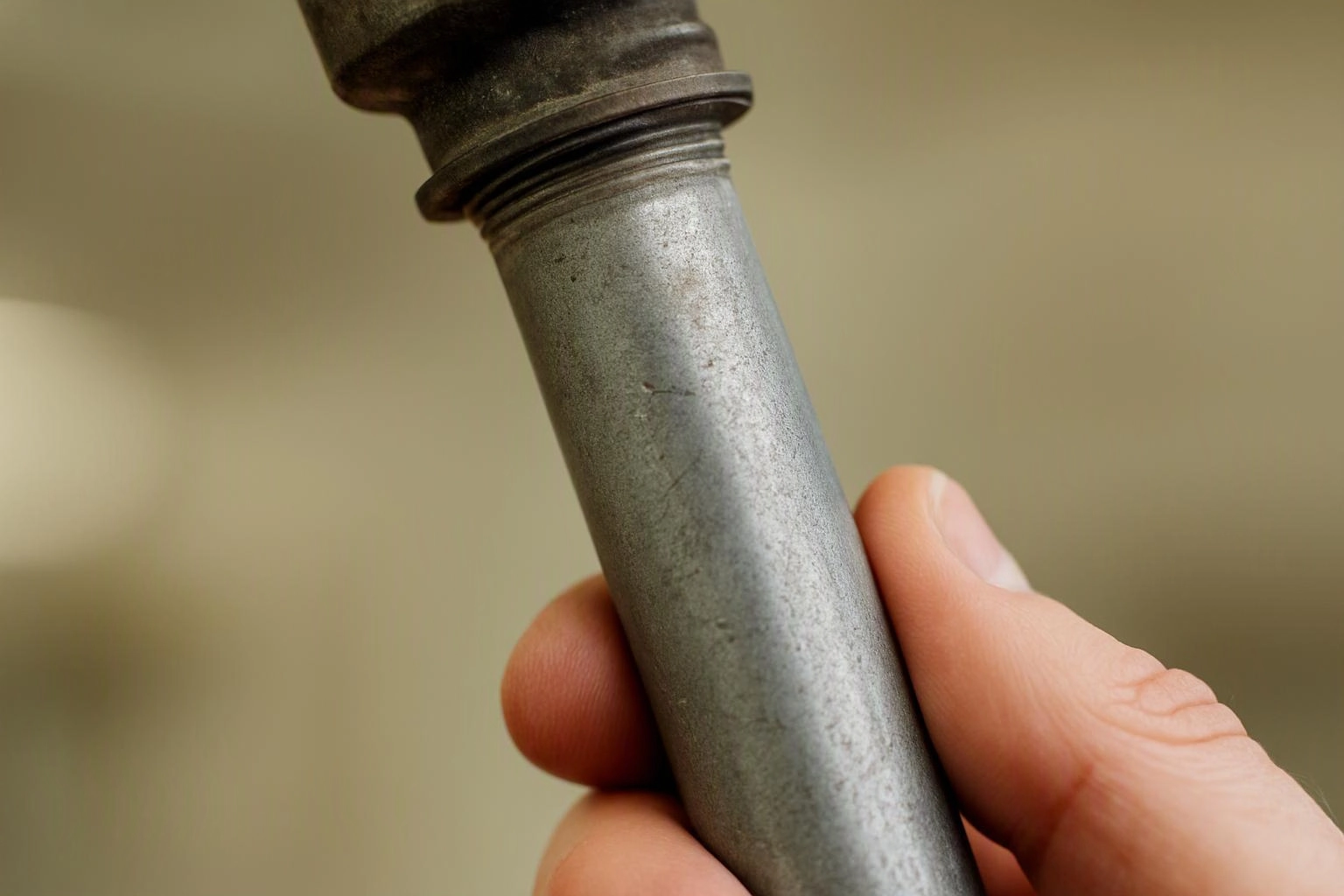 A hand holds a worn metal pipe fitting against a plain beige background