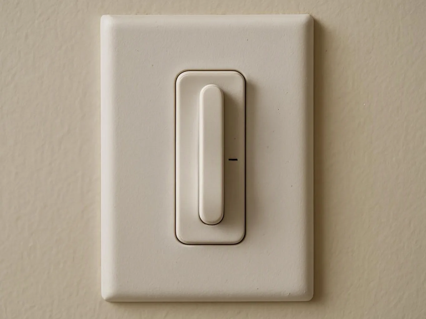 A white wall light switch sits on a beige painted wall, centered in the frame